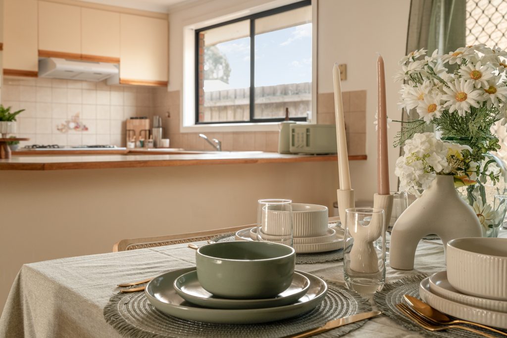 Stylish kitchen and dining setup with a table setting, floral arrangement, and view of a modern kitchen in a real estate property.