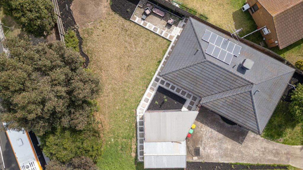 Drone aerial view of a residential property with rooftop solar panels, backyard patio, and surrounding green space.