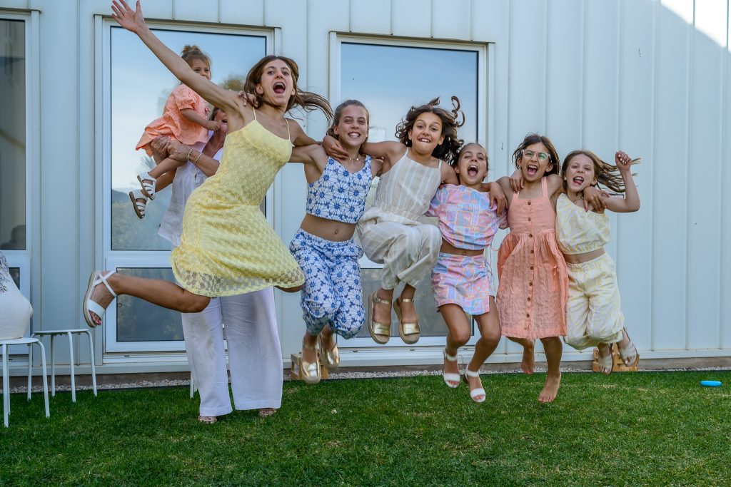 A group of girls laughing and jumping in excitement on a grassy lawn.