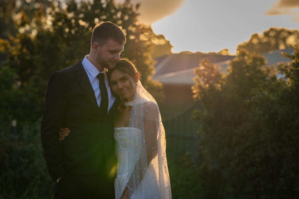 Bride and groom embracing among trees in golden evening light