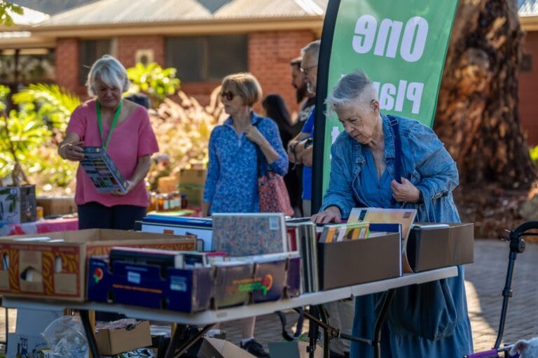 Visitors browsing a colourful community market stall at One Planet Market