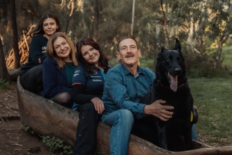 Family portrait with their black dog seated together in an Adelaide park