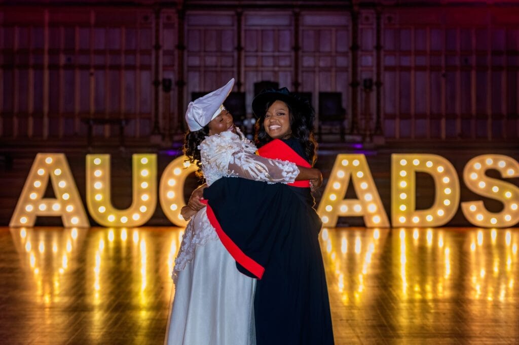 The graduate embracing her mother in the purple-lit graduation hall