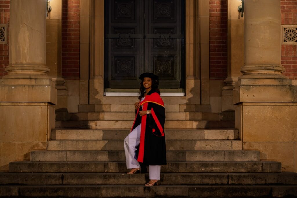 The graduate in regalia on steps between sandstone university columns